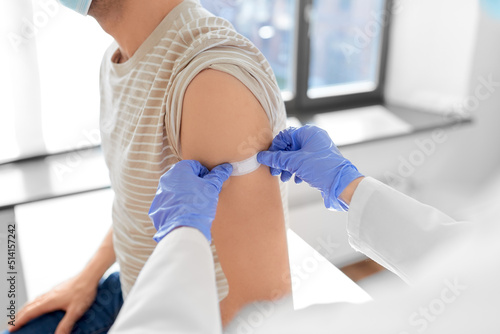 health  medicine and pandemic concept - female doctor or nurse in protective medical mask and gloves sticking patch to patient s hand after vaccination at hospital