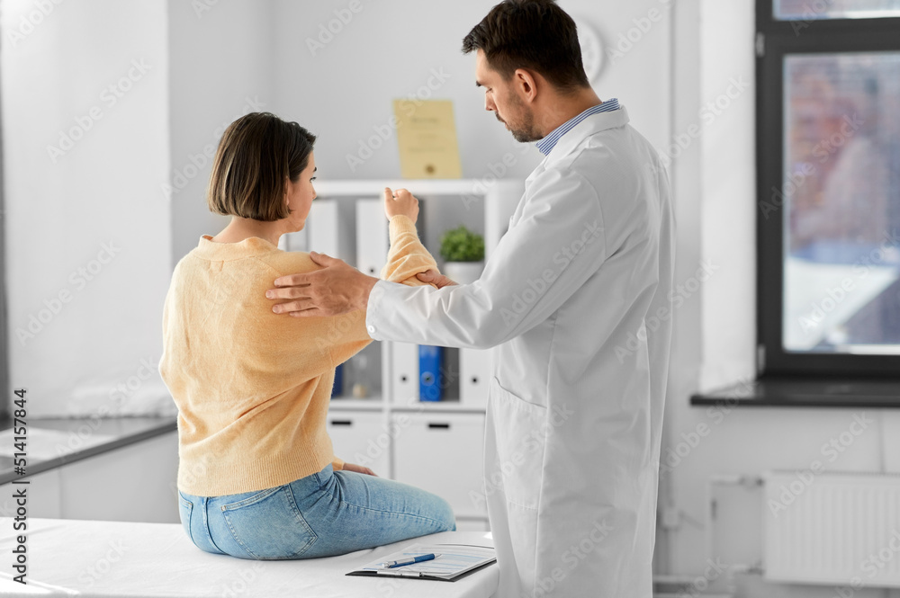 Fototapeta premium medicine, healthcare and people concept - male doctor with clipboard talking to woman showing her sore arm patient at hospital