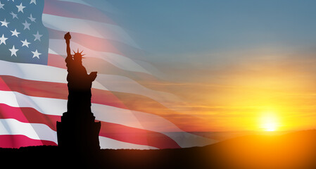 Statue of Liberty with a large american flag and sunset sky on background.