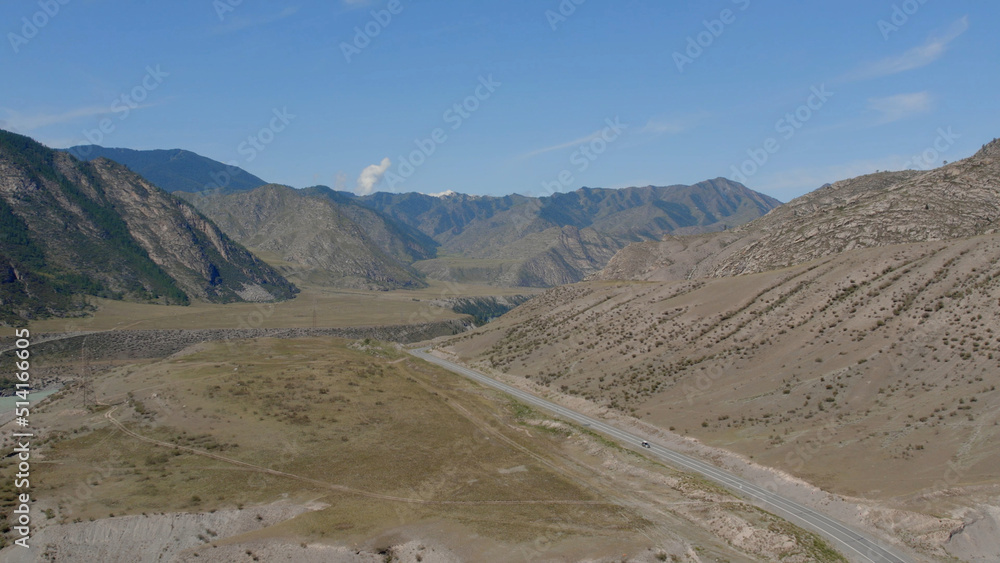 Traffic cars on road between mountains of Altai under clear blue sky
