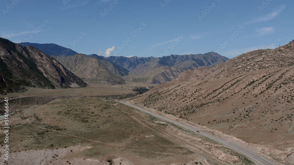 Traffic cars on road between mountains of Altai under clear blue sky