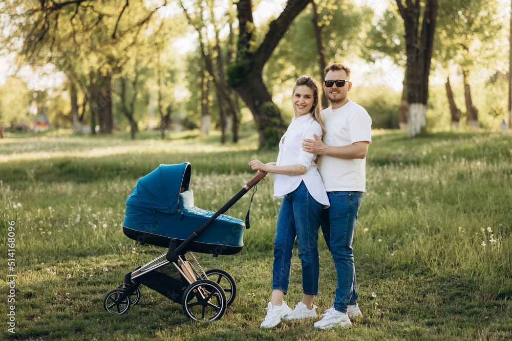 A young family walk in the park in with a toddler in a stroller. Happy parents A young family walk in the park in with a toddler in a stroller. Happy parents