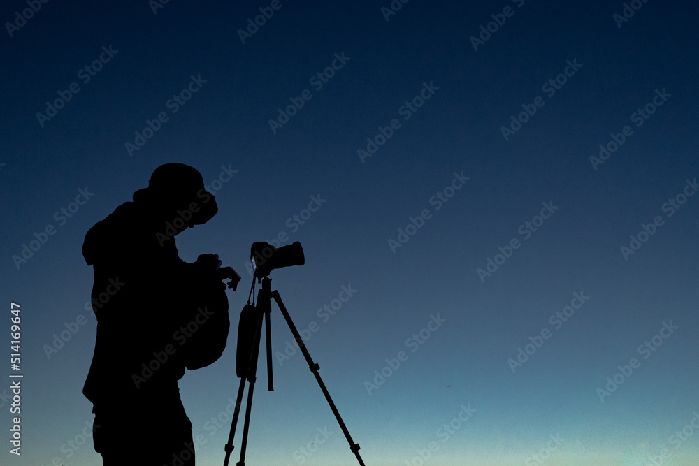 Silhouette of the photographer with tripod. Young man taking photo with his camera during golden hour.