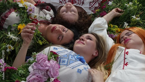 Four beautiful ukrainian girls lying on the grass, top view. Ukrainian girls in national vyshyvanka costumes and wreaths from flowers. Ethnic Ukrainian costume. Patriotic themes