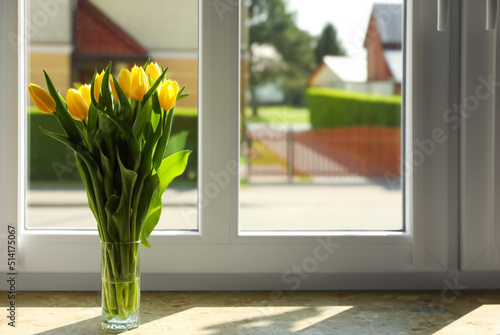 Bouquet of beautiful yellow tulip flowers in glass vase on windowsill. Space for text