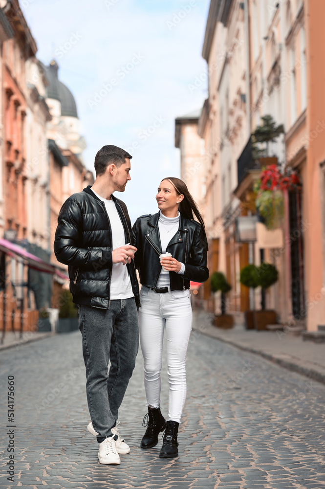 Lovely young couple with cups of coffee walking together on city street. Romantic date