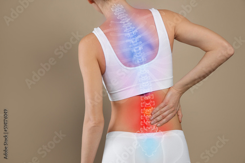 Woman suffering from pain in back on beige background, closeup