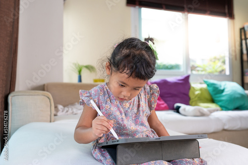 Adorable girl sitting on couch using tablet at home. Home learning concept.