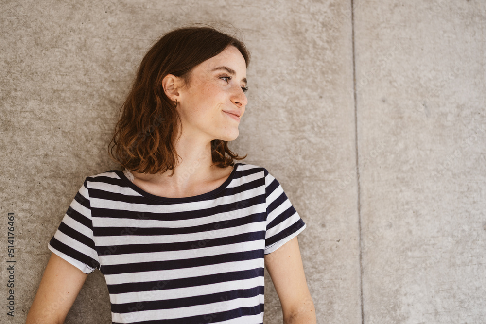 Young smiling woman stands in front of modern brown wall and looks to the side Young smiling woman stands in front of modern brown wall and looks to the side