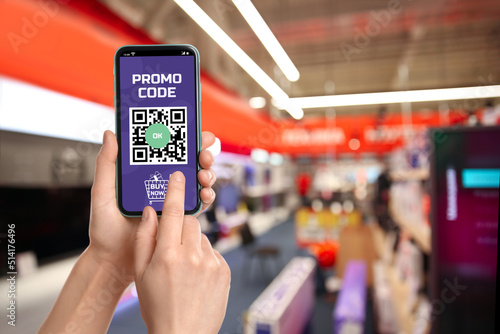 Woman holding smartphone with activated promo code in shopping mall, closeup