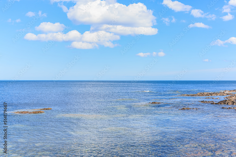 A scenic view of a rocky Scottish shore with crystal blue water under a majestic blue sky and some huge white clouds