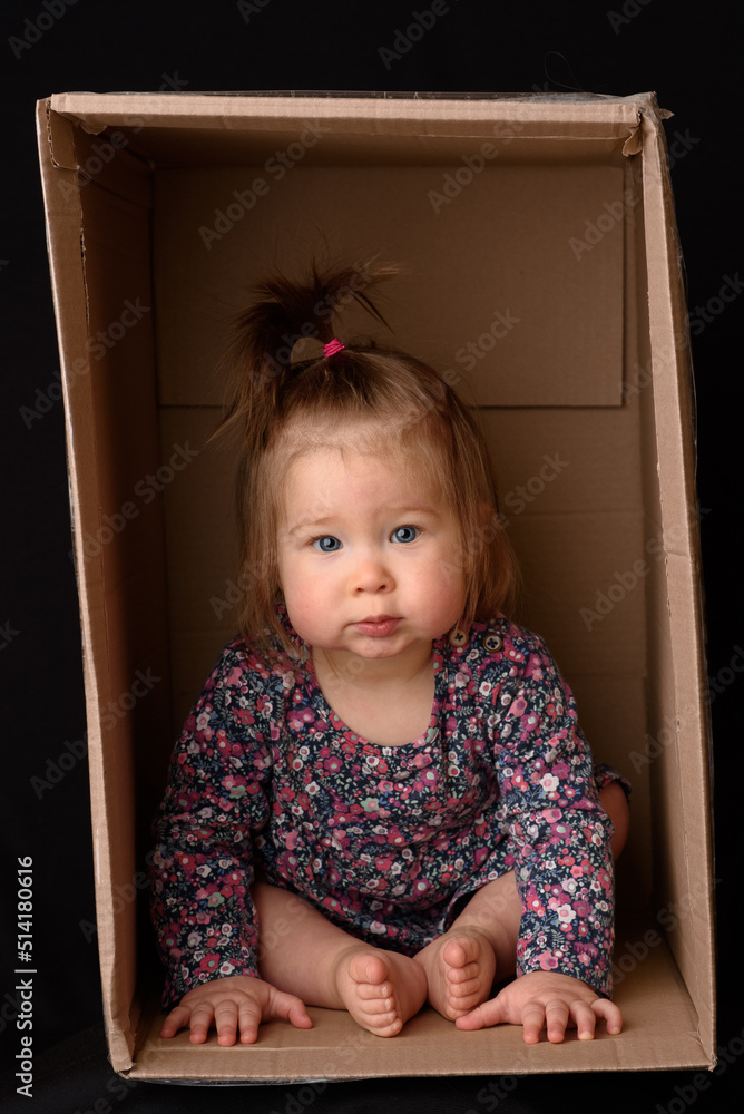Happy little girl sitting in a cardboard box and having fun Happy little girl sitting in a cardboard box and having fun