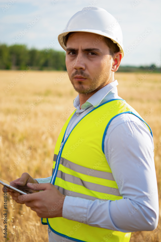 Fototapeta premium an engineer with a tablet in his hands stands in the middle of a green field, an agronomist in a field with wheat checks the harvest, summer day, smart farm, farming activities, eco products.