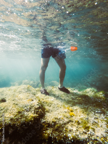 Legs of a boy on top of a rock in the sea, with a snorkel mask in his hand