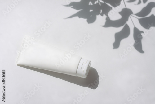 Cosmetic bottle with leaf shadow on white wall background