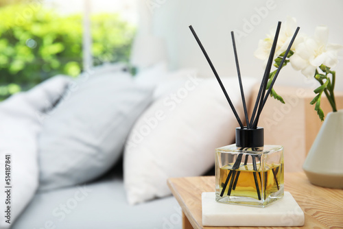 Reed diffuser and vase with bouquet on wooden nightstand in bedroom. Space for text photo