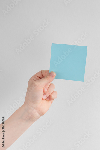 child hand holding a square blue blank reminder or paper notes above a white and gray background, copy space
