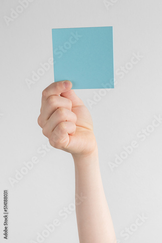 child hand holding a square blue blank reminder or paper notes above a white and gray background, copy space