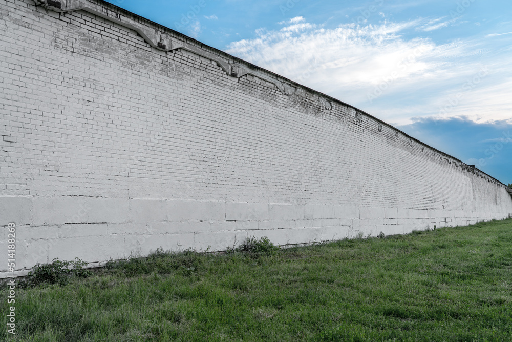 Long spacious empty old white colored brick wall structured on green grass against blue sky Long spacious empty old white colored brick wall structured on green grass against blue sky