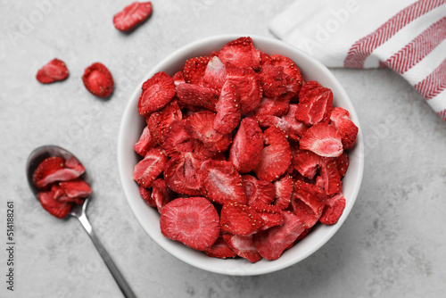 Bowl and spoon with dried strawberries on light grey table, flat lay photo