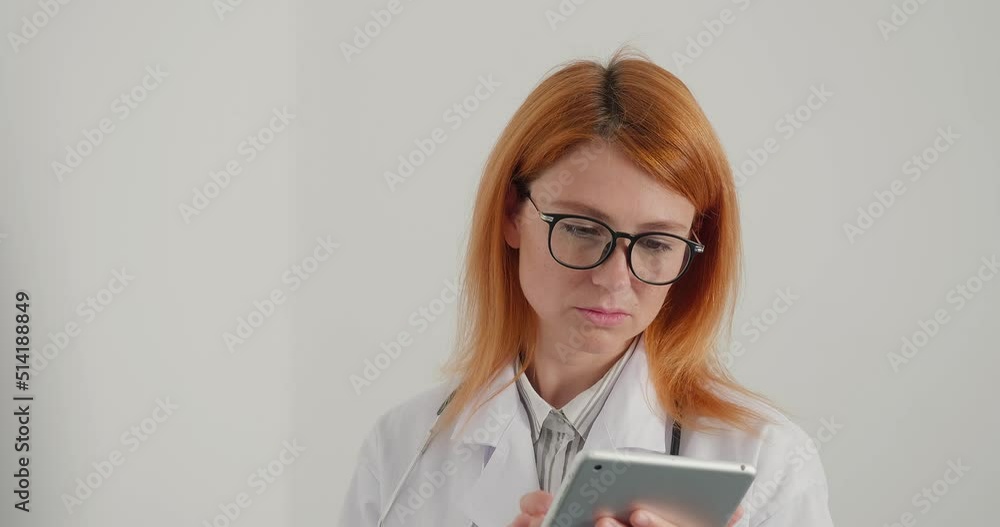 Red-haired woman doctor in glasses works on tablet in office Red-haired woman doctor in glasses works on tablet in office