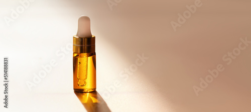 Cosmetic amber glass dropper bottle with oil, serum or fruit peeling in the sunlight on beige background with soft focus. Beauty product presentation, natural banner. Front. Mockup concept 