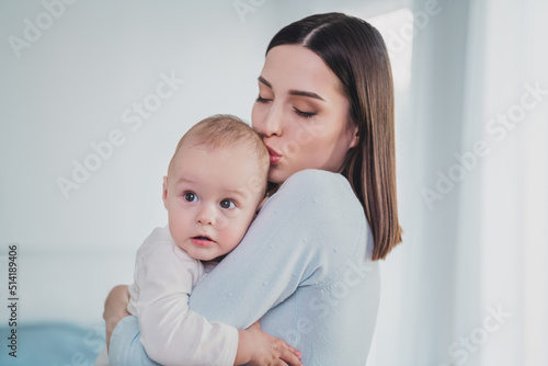 Portrait of charming peaceful lady hold kiss head adorable toddler support trust house indoors