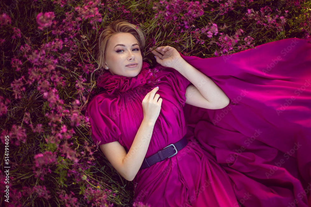 portrait fashionable beautiful young woman lying in a pink dress in a field with wildflowers in summer at sunset. portrait fashionable beautiful young woman lying in a pink dress in a field with wildflowers in summer at sunset.