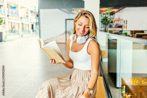 A cropped shot of a young elegant business woman reading a book in a mall while enjoying coffee. Book in woman hands.