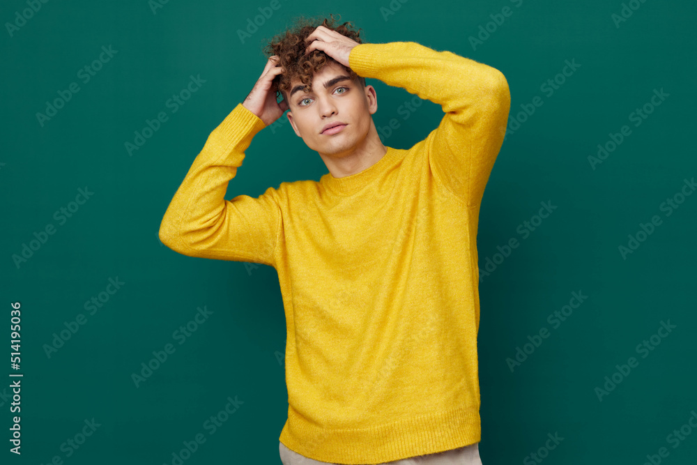 a handsome man stands on a green background in a yellow sweater and straightens his curly hair with his hands . Horizontal photo with empty space a handsome man stands on a green background in a yellow sweater and straightens his curly hair with his hands . Horizontal photo with empty space