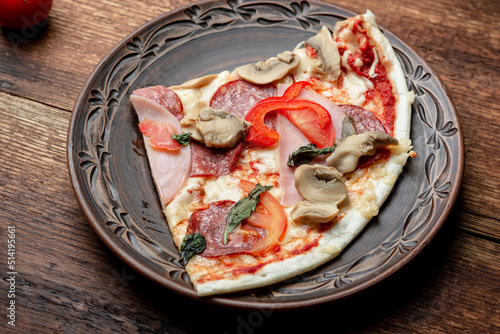 Pizza with ham and bacon, mushrooms on a clay plate on a brown wooden background.