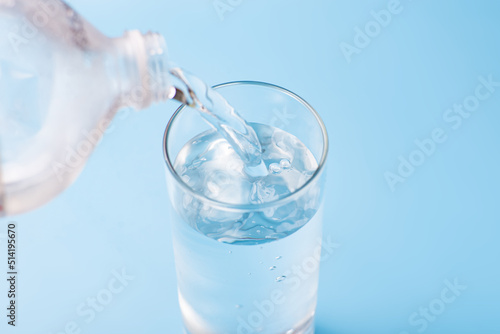 Water pours into a glass of clean cold water on a blue background.