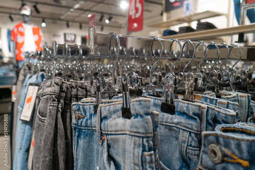Many jeans of different colors hang on hangers in the store. Concept of buying, selling, shopping and denim fashion.