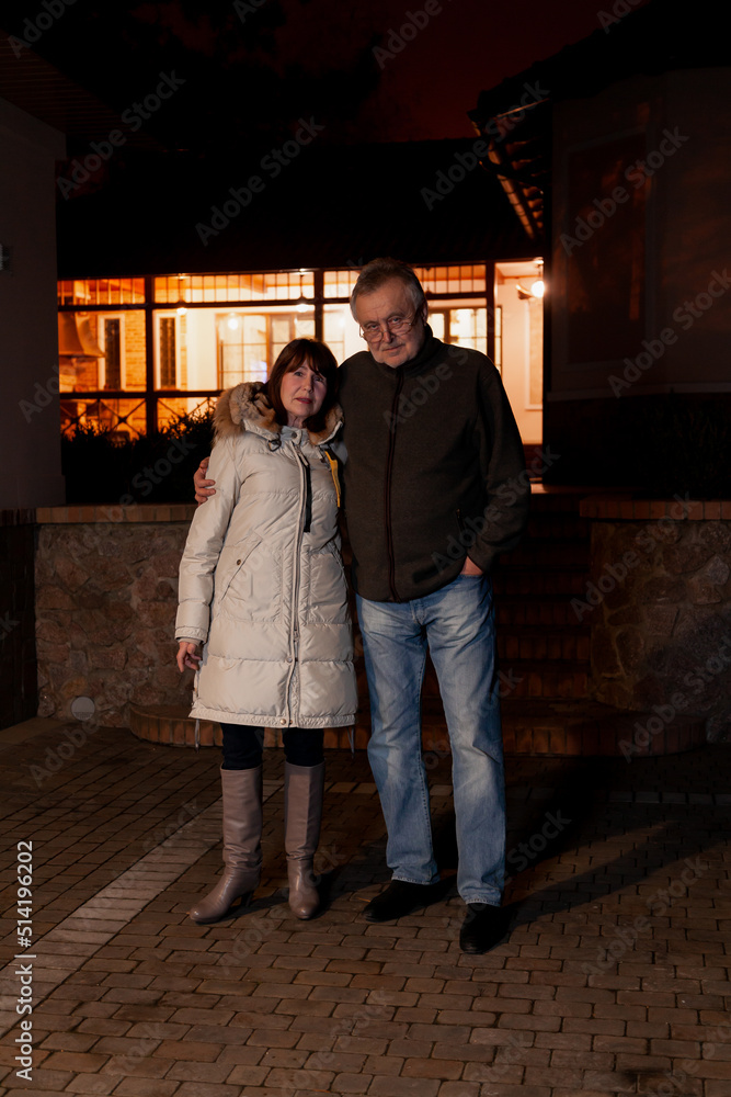 elderly couple standing in courtyard of house on autumn evening....