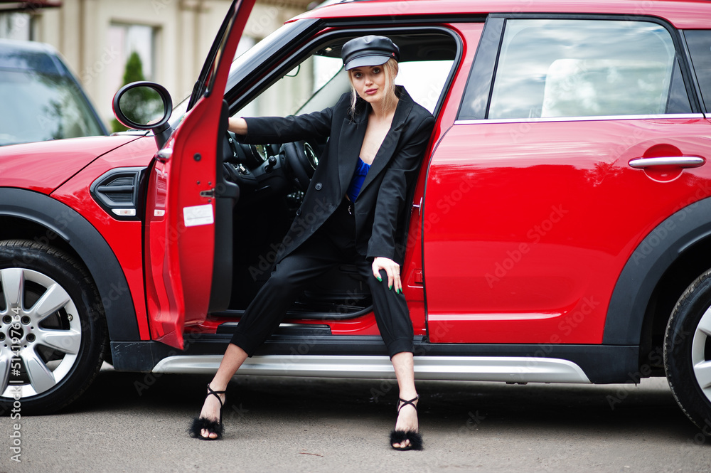 Portrait of beautiful blonde sexy fashion woman model in cap and in all black, blue corset, with bright makeup near red city car.