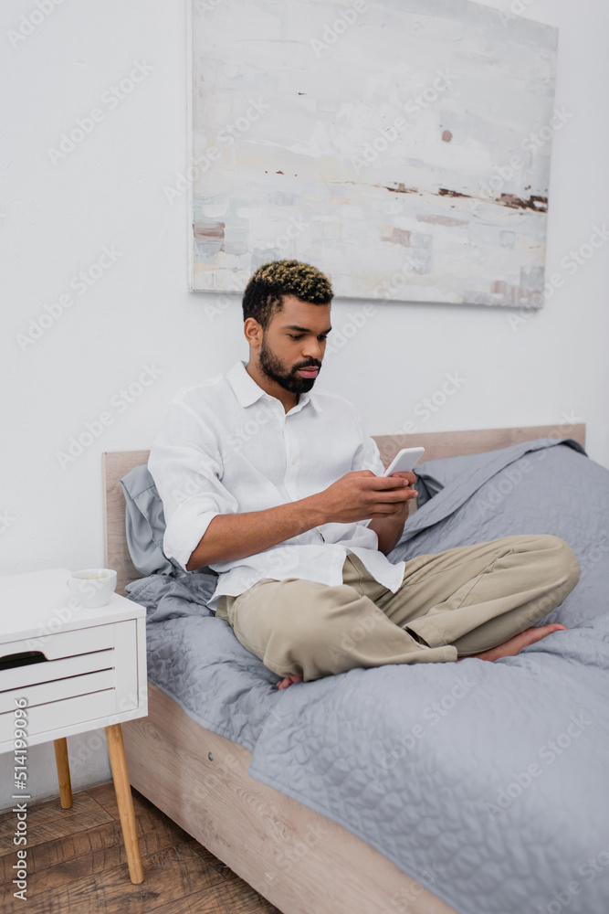young african american man with dyed hair using smartphone while resting on bed.