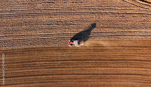Tracteur isolé travaillant dans un champ en terre après le labour. Silhouette et trainée de poussière visible.