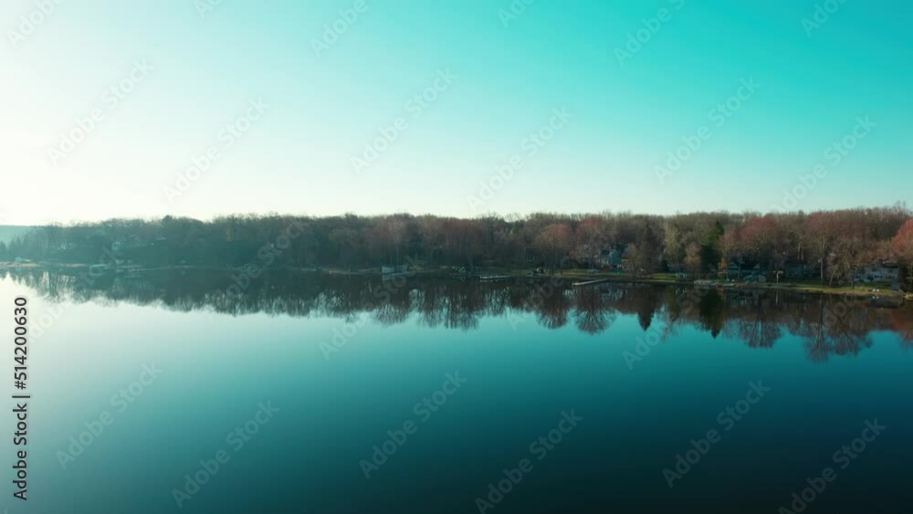 Drone going sideways showing the beautiful wooded shore of the blue lake with reflections over still water Drone going sideways showing the beautiful wooded shore of the blue lake with reflections over still water