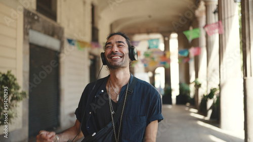 Young italian guy with ponytail and stubble in headphones goes to the city landscape background. Stylish guy listens to music in headphones photo