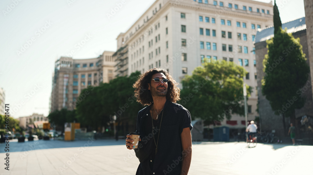 Young italian guy with long curly hair and stubble is enjoying aromatic coffee. Stylish man drinks coffee on old town background Young italian guy with long curly hair and stubble is enjoying aromatic coffee. Stylish man drinks coffee on old town background