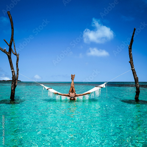 Beautiful sexy tanned woman in white bikini on Maldives island. Young glamour girl is posing on hammock in paradise . Perfect body bikini model on Maldives beach. Bikini fashion. Luxury travel.