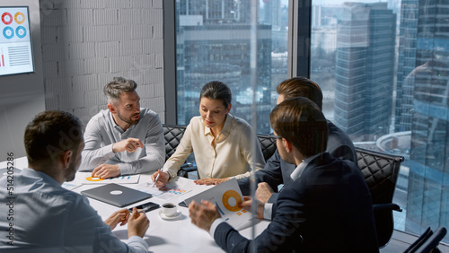 Corporate businesswoman communicating with team while sitting at desk in meeting room