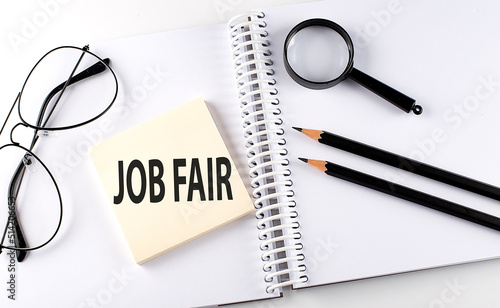 Word JOB FAIR on the sicker on the notebook with pencils,magnifier and glasses