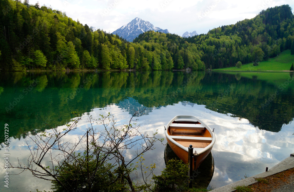 a boat resting on the tranquil, transparent emerald-green water of lake Alatsee in the Bavarian Alps reflected in the lake, Fussen or Fuessen in Bavaria, Germany	