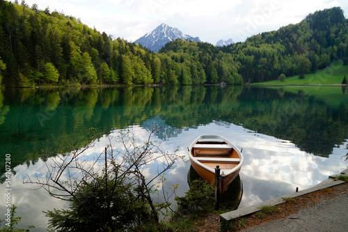 a boat resting on the tranquil, transparent emerald-green water of lake Alatsee in the Bavarian Alps reflected in the lake, Fussen or Fuessen in Bavaria, Germany 