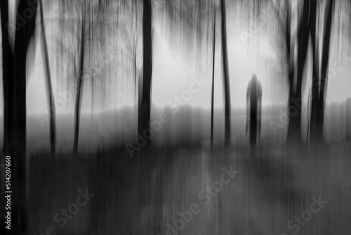Creative textured black and white image in motion blur of phantom walking among trees in the fog.