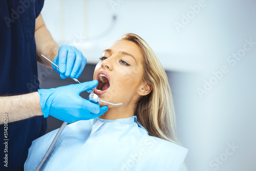 Closeup shot professional dentist with protective surgical mask  doing check up of patient. Dentist examining smiling female patient in clinic. Male is checking smiling patient in examination room.