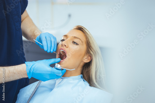 Perfect smile! Part of dentist examining his beautiful patient in dentist office. European young woman smiling while looking at mirror in dental clinic