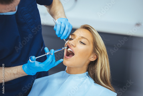 Close up of dentist s hands holding tool and syringe in hands. Pain killer in action. Female client keep mouth opened. Beautiful smile and white teeth. Cut view.