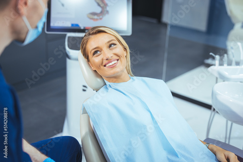 Pretty lady in dentist chair looking at her doctor with smile, close up. Image of pretty young woman sitting in dental chair at medical center while professional doctor fixing her teeth..